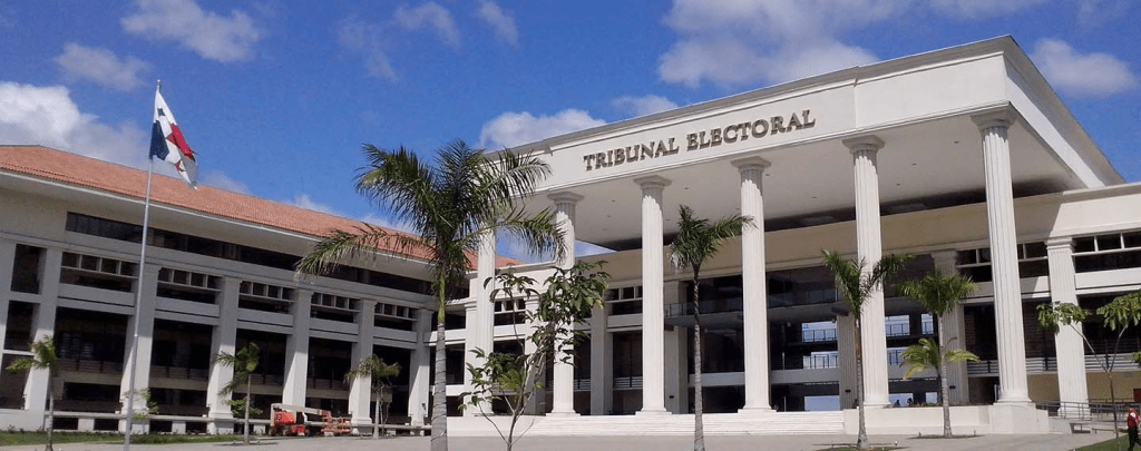 Edificio del Tribunal Electoral de Panamá, con columnas y banderas, el cielo despejado de fondo.