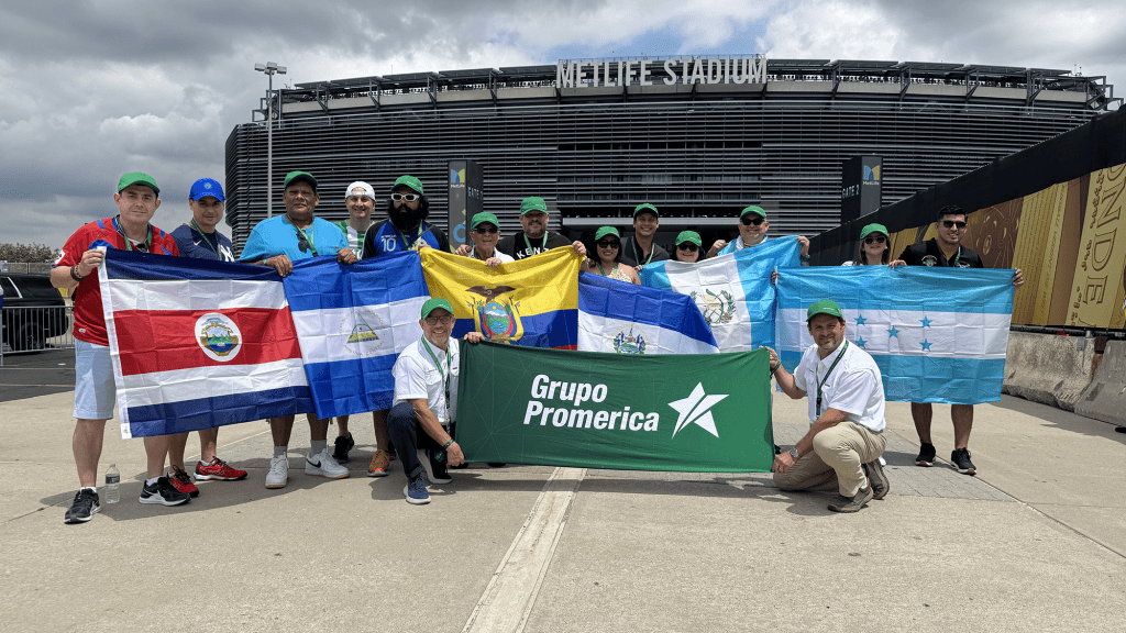 Grupo Promerica employees and clients holding various national flags in front of MetLife Stadium, celebrating the tenth anniversary of Experiencias Promerica.