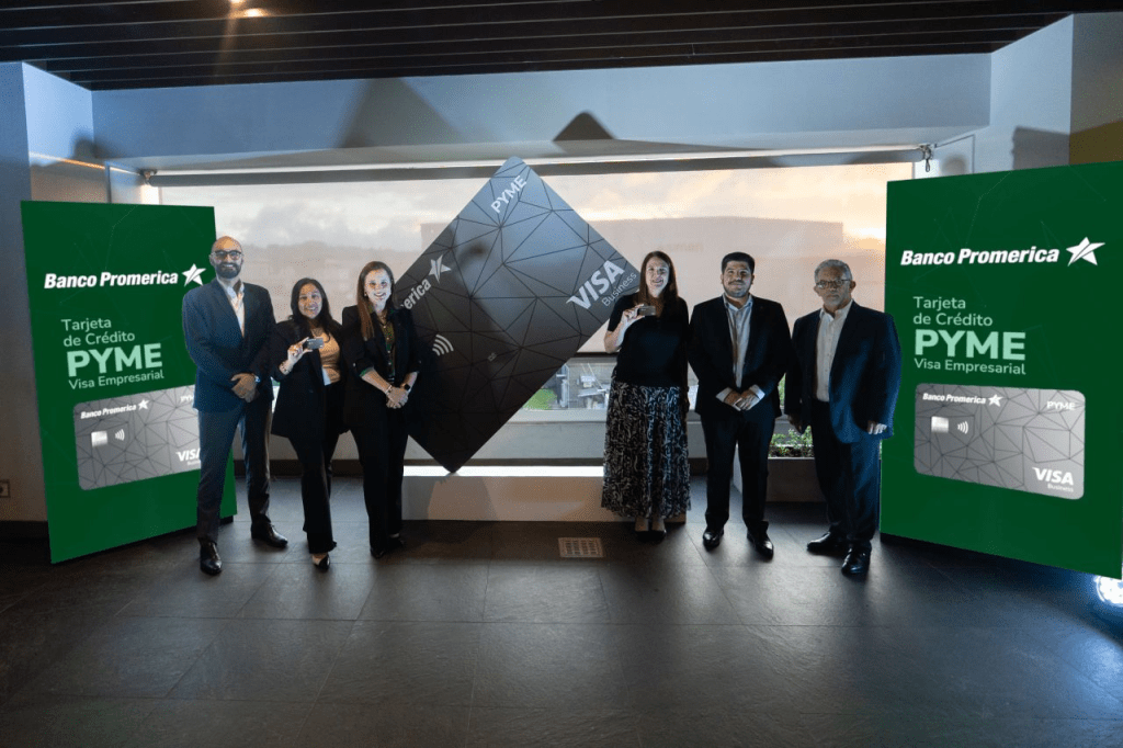 Grupo de personas posando con la tarjeta de crédito PYME Visa Empresarial de Banco Promerica, junto a carteles informativos sobre la tarjeta.
